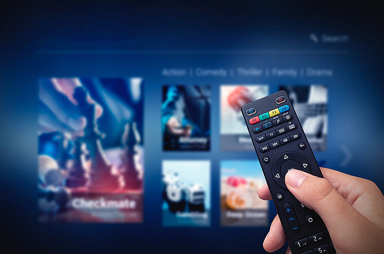 Hand mit Fernbedienung vor Smart-TV Bildschirm