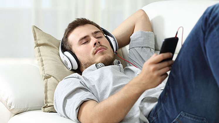 Junger Mann auf Sofa hört Musik
