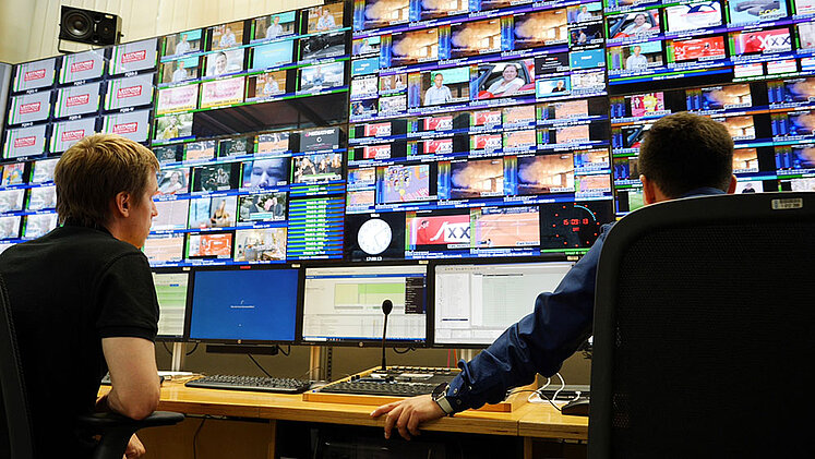 Techniker schauen auf viele Monitore im ORS-Broadcastcenter